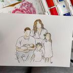 A watercolor painting of a family on a white sheet of paper, shown in front of an open watercolor palette with mixed paint colors.